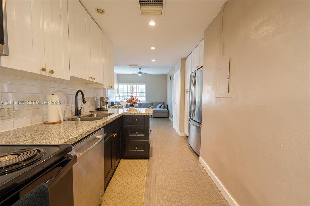 Kitchen featuring two-tone shaker-style cabinetry, stone-finish countertops, subway tile backsplash, stainless steel appliances, and wood-finish tile flooring