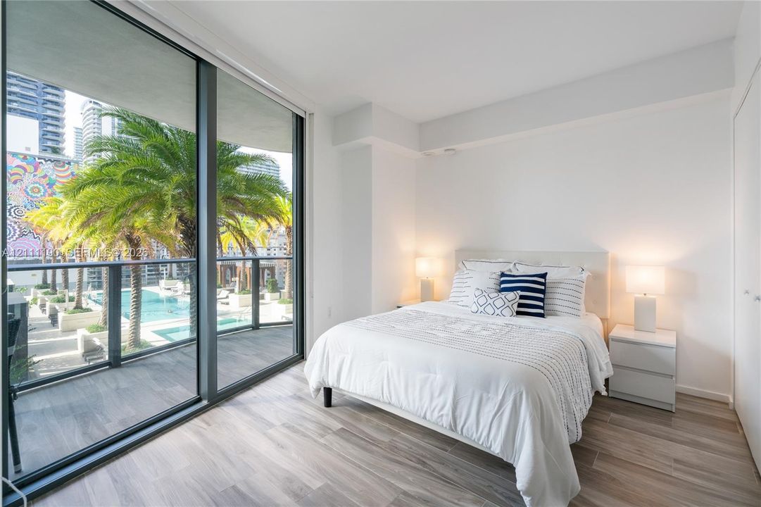 Floor-to-ceiling glass sliding doors, private balcony with metal railing, wood-finish flooring, and neutral wall finishes