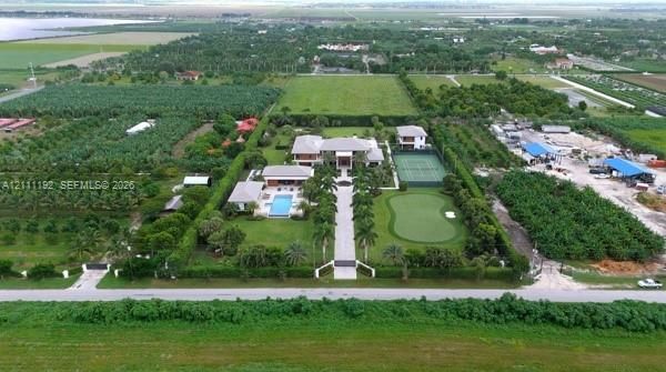 Aerial perspective of a sprawling estate featuring a paved entry driveway, an in-ground swimming pool, a private tennis court, and a dedicated putting green