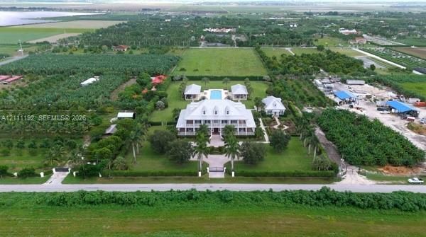 Multi-structure estate featuring a multi-story residence with a metal roof, detached garage buildings, a swimming pool, and gated entry, all situated on expansive acreage with extensive landscaping