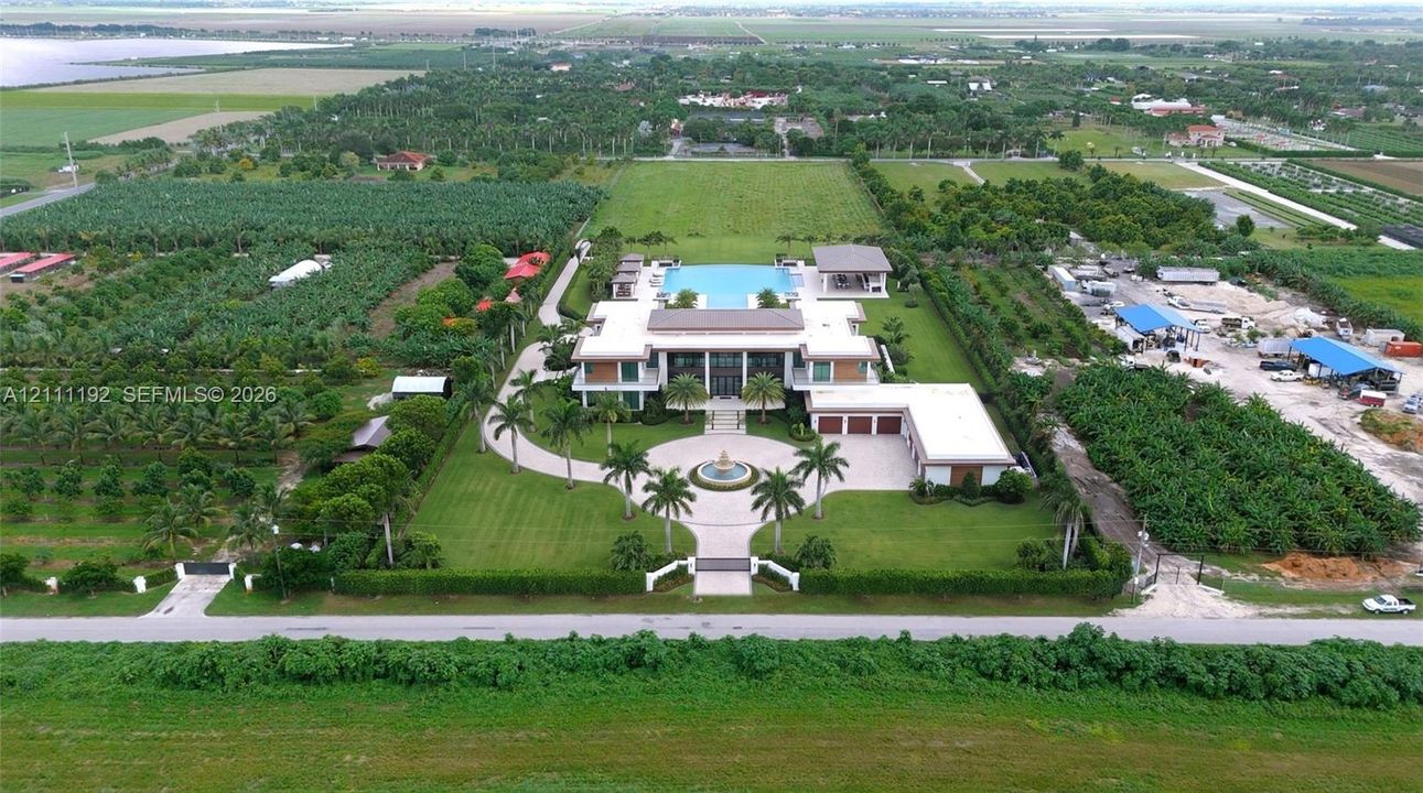 Aerial perspective of a sprawling estate featuring a paved circular driveway, center courtyard fountain, swimming pool, and multi-car garage on expansive grounds