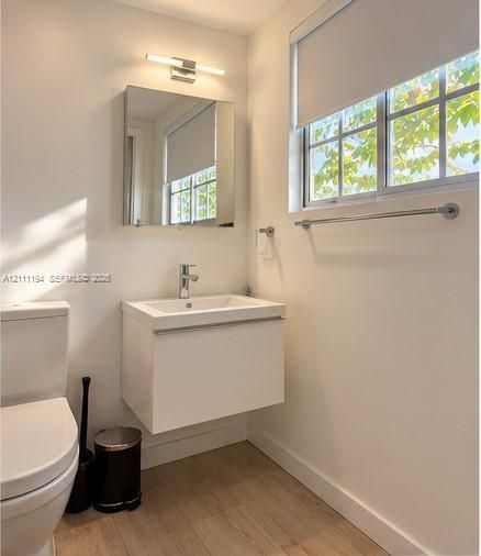 White floating vanity with integrated sink, rectangular medicine cabinet, wall-mounted light fixture, and wood-finish flooring