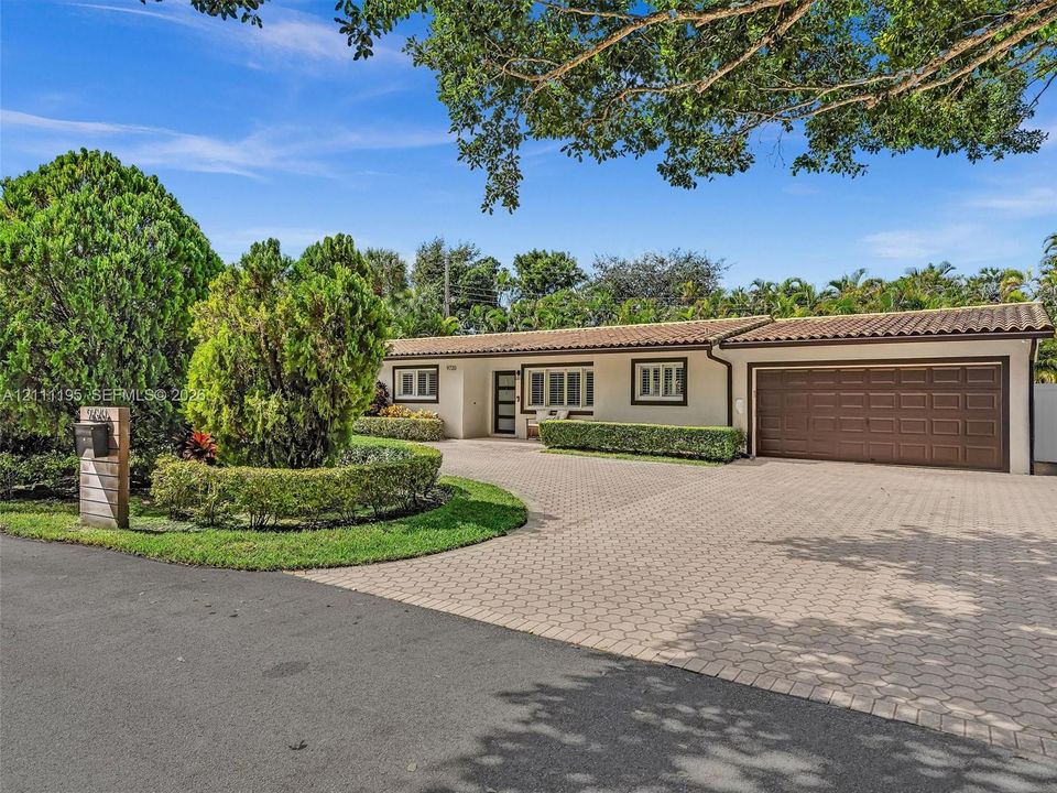 Single-story residence featuring a tile roof, an expansive paved driveway, an attached garage, and manicured landscaping