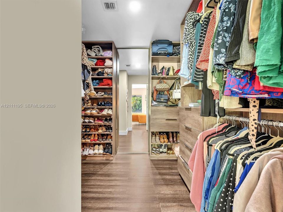 Custom walk-in closet featuring wood-finish cabinetry, built-in shelving, integrated dresser drawers, and wood-finish flooring