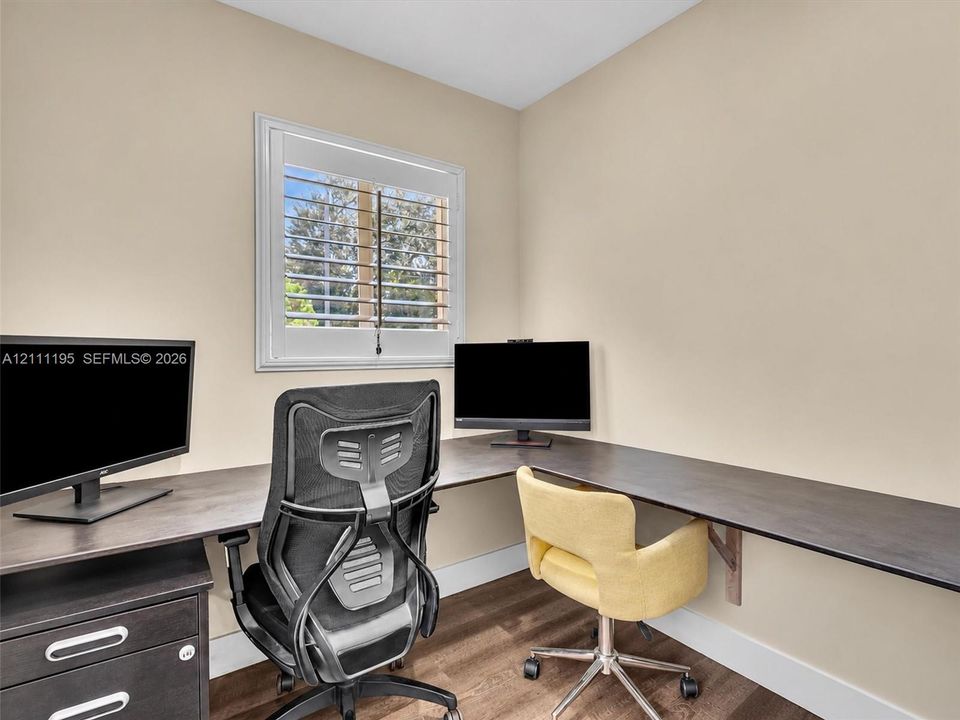 Built-in corner desk with a dark wood-finish surface, wood-finish flooring, and white plantation shutters