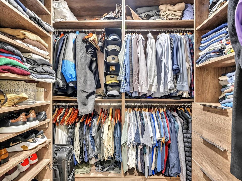 Custom reach-in closet featuring wood-finish shelving, multiple hanging rods, and built-in drawers with metallic hardware