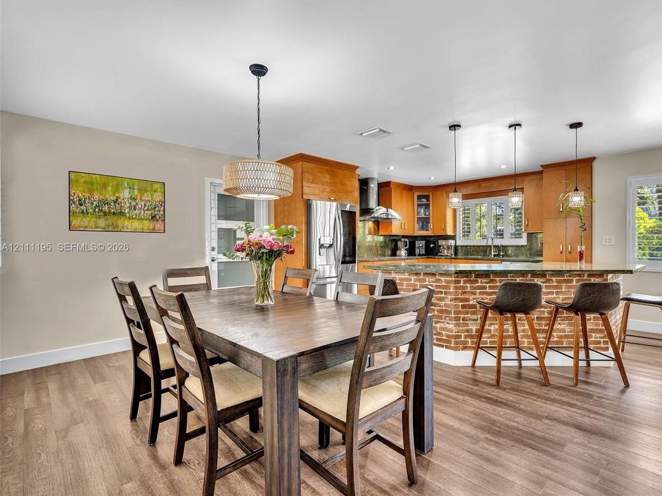 Kitchen featuring a brick-accented peninsula, wood-finish flooring, wood cabinetry, stainless steel refrigerator, and hanging pendant lighting