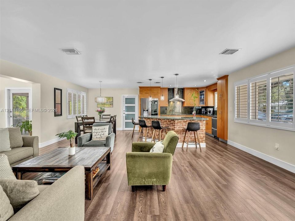 Open-concept floor plan featuring wood-finish flooring, brick-accented kitchen island, custom cabinetry, and plantation shutters