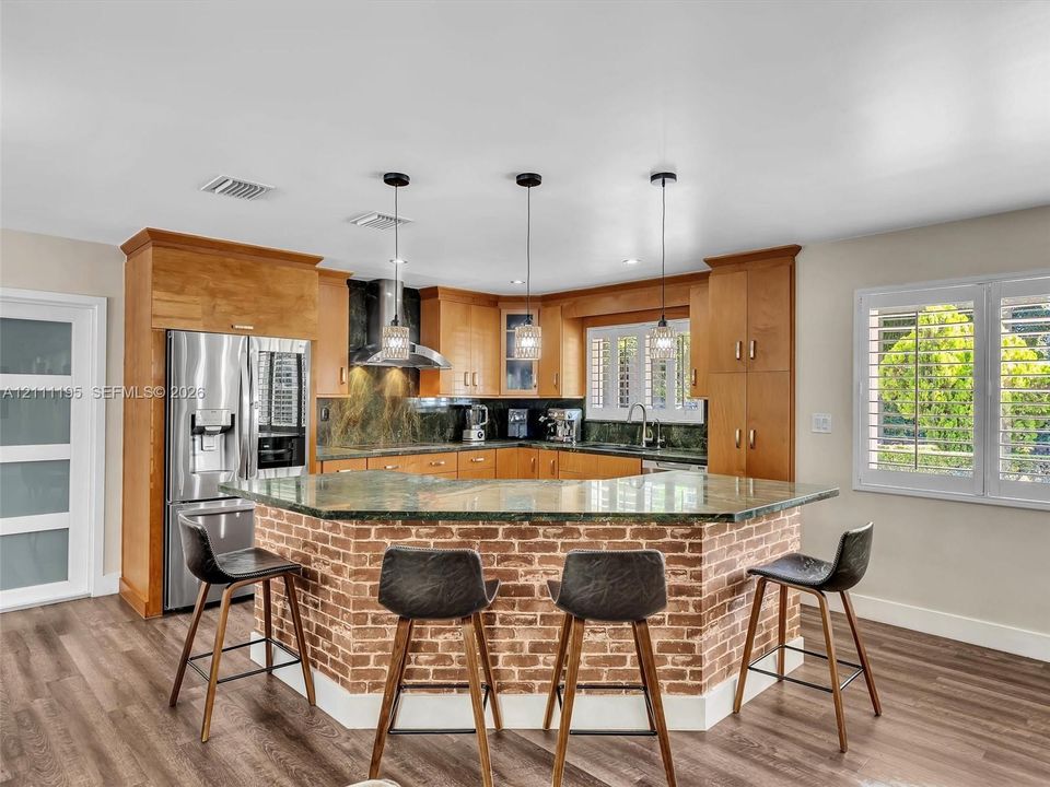 Kitchen featuring custom wood cabinetry, a stone-topped island with a brick facade, stainless steel appliances, and multi-pendant lighting