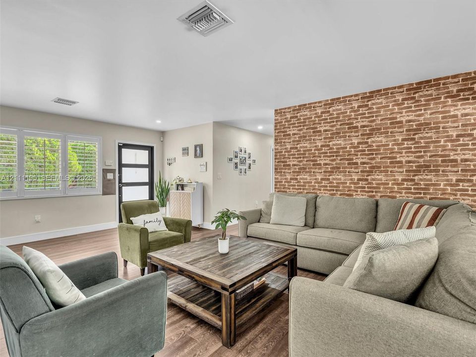 Exposed brick accent wall, wood-finish flooring, multi-pane window with plantation shutters, and glass-paneled entry door