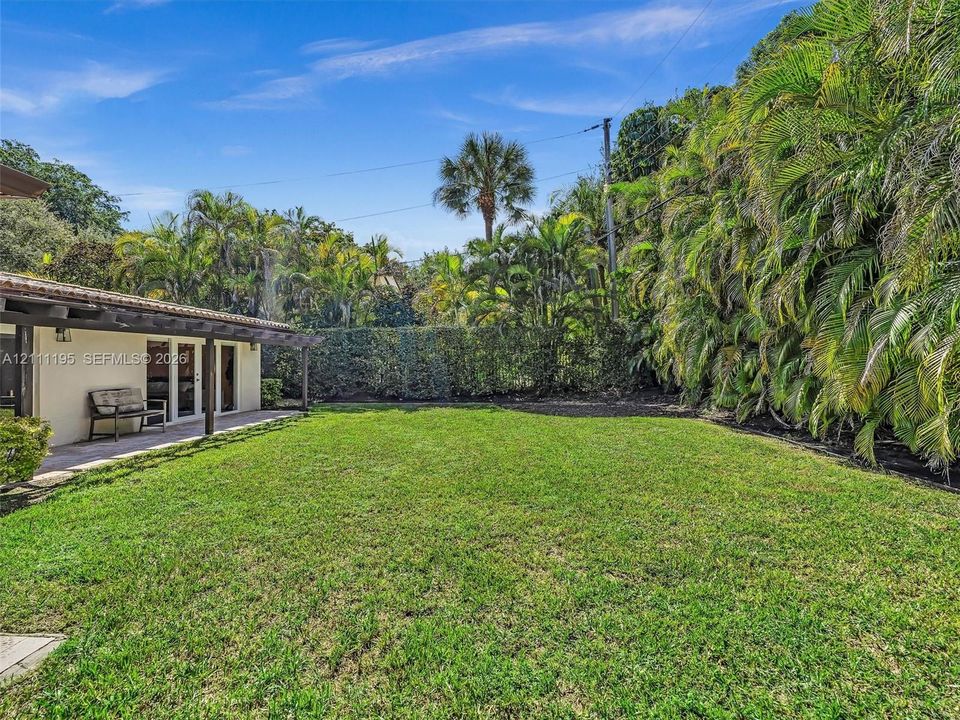 Rear exterior featuring a covered patio, pergola structure, expansive lawn, and mature palm landscaping