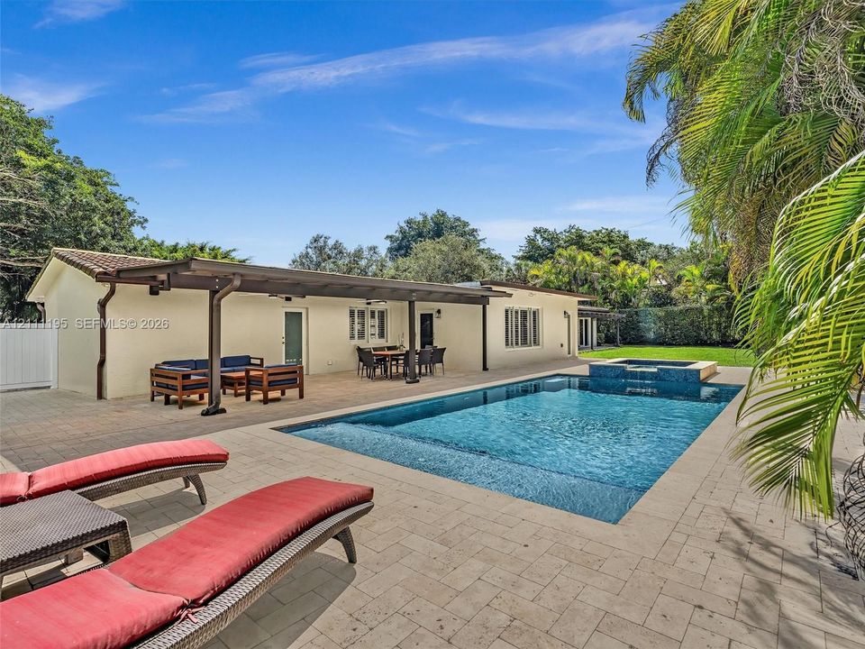 Outdoor living area featuring a covered patio with tile flooring, an inground pool with an integrated spa, and extensive paver decking