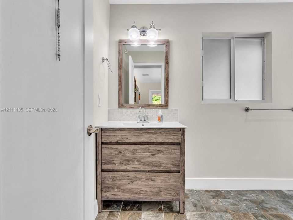 Wood-finish vanity with a rectangular sink, quartz countertop, mosaic tile backsplash, wood-framed mirror, and multi-light vanity fixture