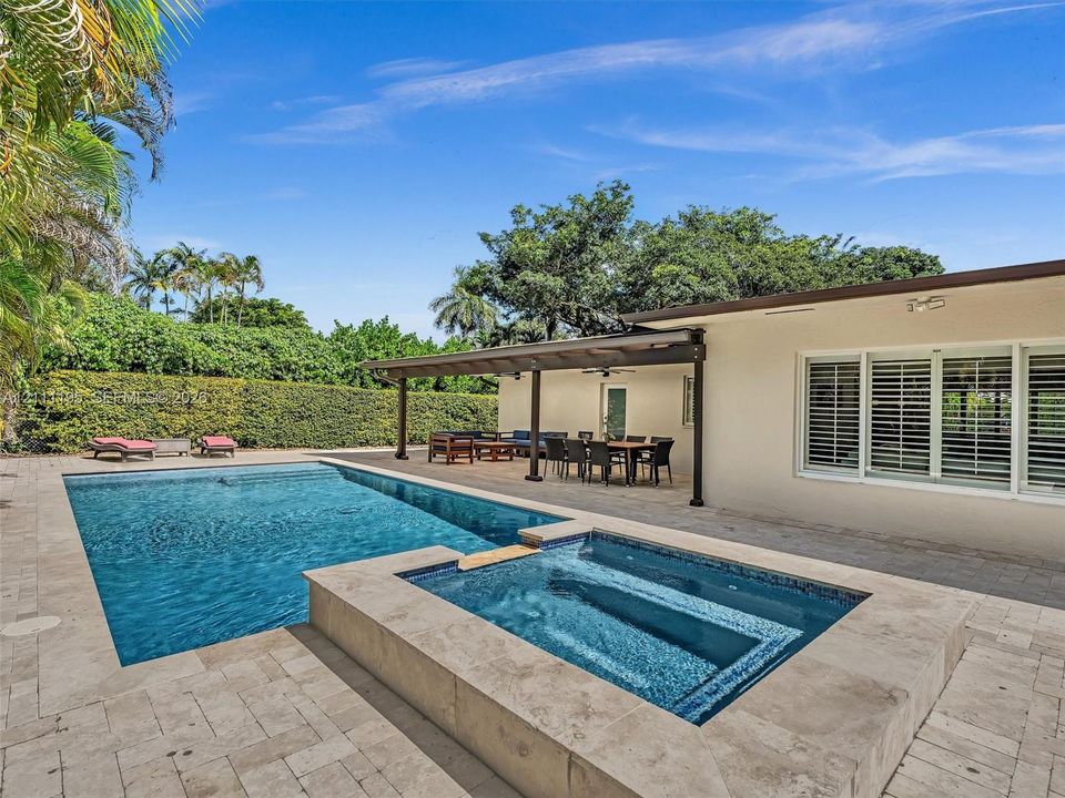 Outdoor living space featuring an in-ground swimming pool, raised spa, stone-paver decking, and a covered patio area