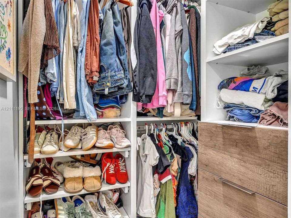 Custom closet organization featuring multi-level hanging rods, built-in shelving, and drawers with wood-finish fronts and minimalist metal pulls