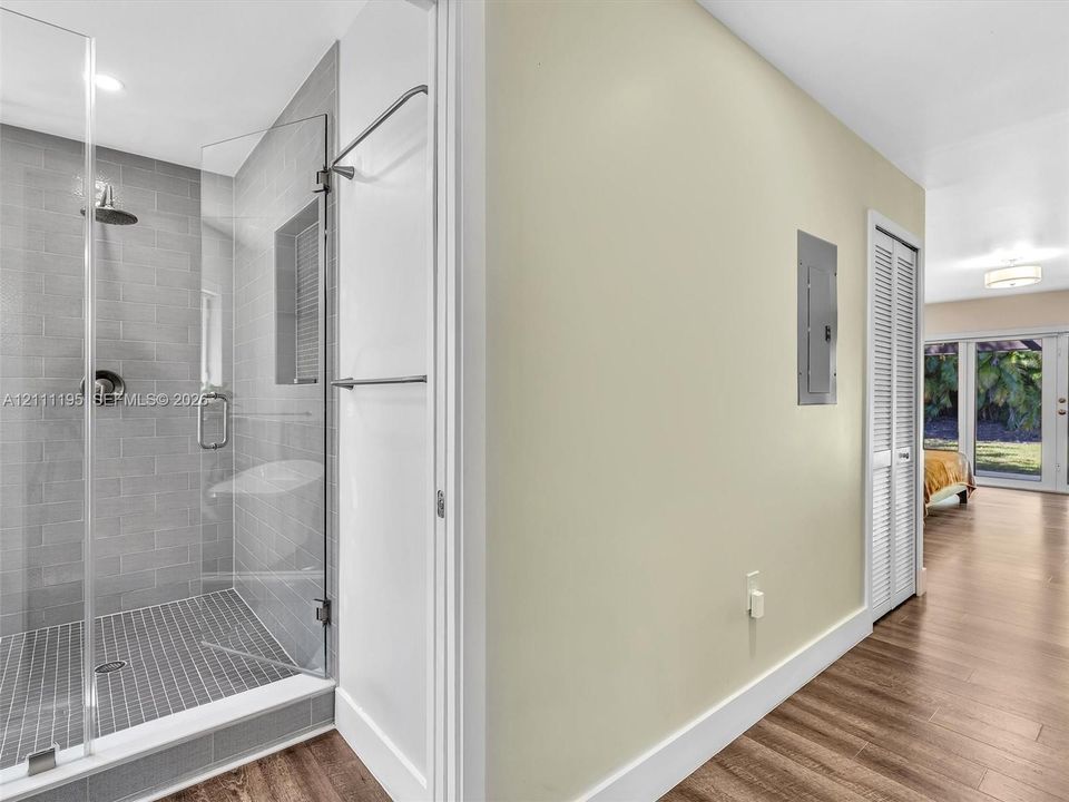Walk-in shower featuring grey subway tile, mosaic floor tile, glass enclosure, and a ceiling-mounted rainfall shower head, complemented by wood-finish flooring and louvered bifold doors