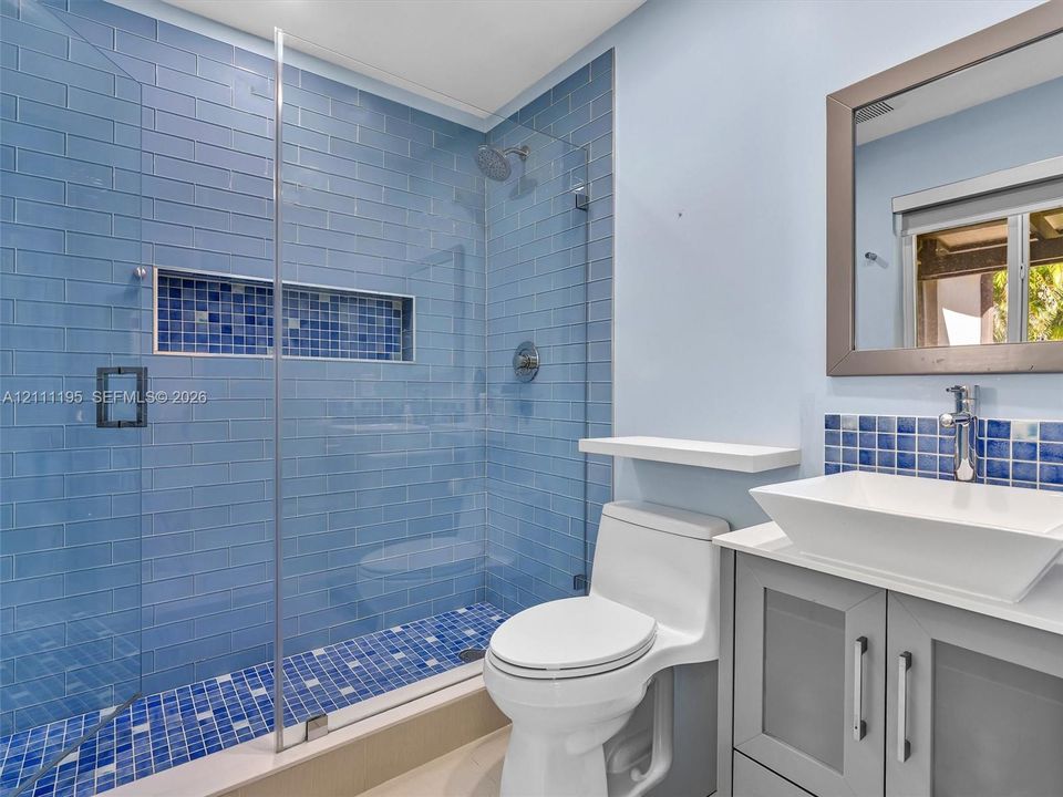 Walk-in shower featuring blue subway-style tile, a decorative mosaic tile inset, and a frameless glass enclosure