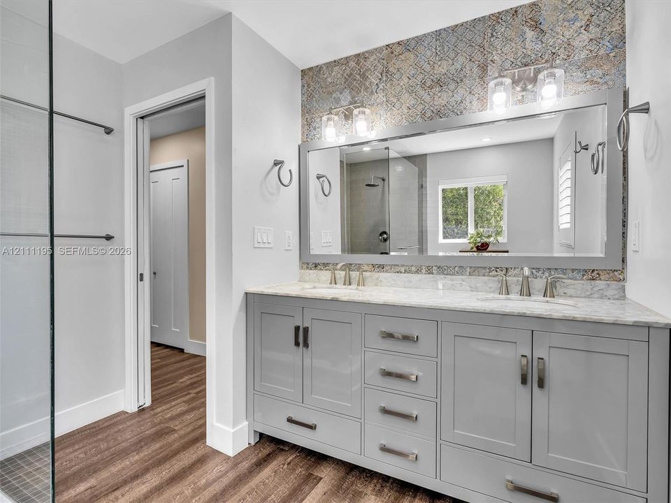 Double vanity featuring light grey cabinetry, stone-finish countertops, dual under-mount sinks, and framed vanity mirror with decorative tiled backsplash