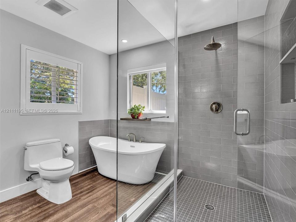 Freestanding soaking tub with polished chrome fixtures, walk-in shower featuring subway tile surround and mosaic tile flooring, glass enclosure, and wood-finish flooring