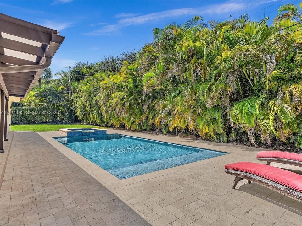 In-ground swimming pool with an integrated spa, surrounded by stone paver decking and extensive perimeter landscaping