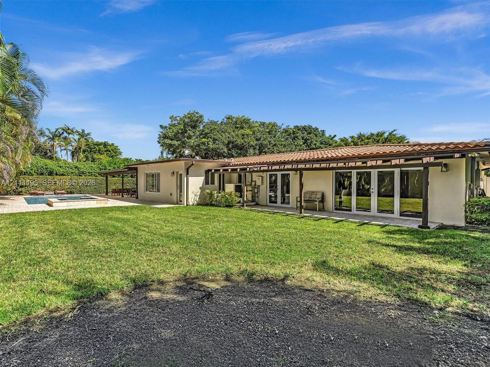 Expansive backyard featuring a manicured lawn, an in-ground swimming pool, a concrete patio, and a covered pergola structure