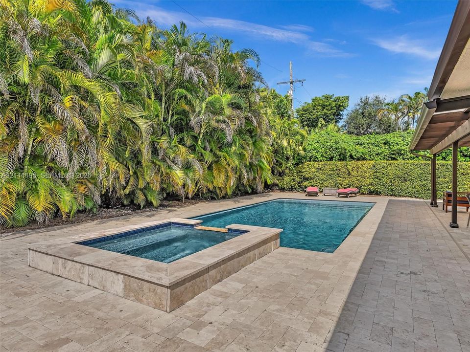 In-ground swimming pool with an integrated elevated spa, finished with stone tile decking and lush privacy hedging