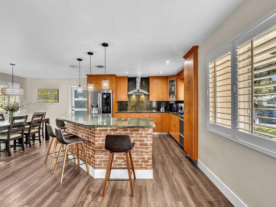 Kitchen featuring an exposed brick breakfast bar, stone countertops, wood-finish flooring, custom wood cabinetry, and stainless steel appliances