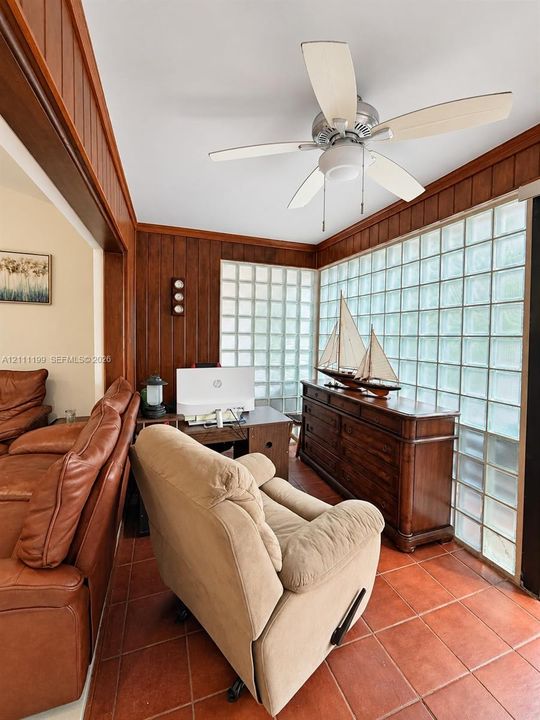 Wood-paneled walls, expansive glass block windows, ceiling fan, and ceramic tile flooring