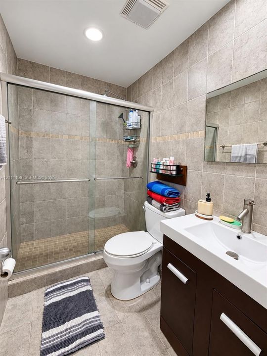 Bathroom featuring a glass-enclosed shower with tiled surround, dark wood-finish vanity, integrated rectangular sink, brushed metal faucet, and wall-mounted vanity mirror