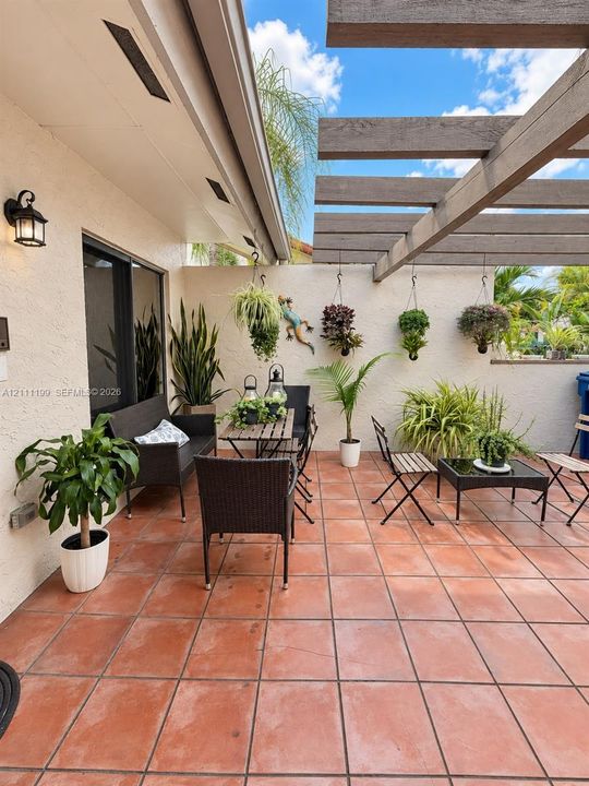 Outdoor patio featuring terracotta tile flooring, a built-in wooden pergola, and exterior wall-mounted lighting