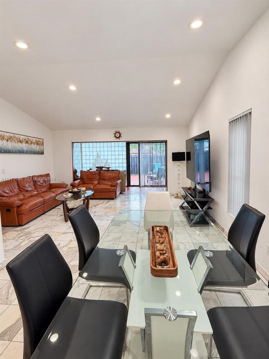 Open-concept room featuring vaulted ceilings, recessed lighting, stone-finish tile flooring, and glass block window accents