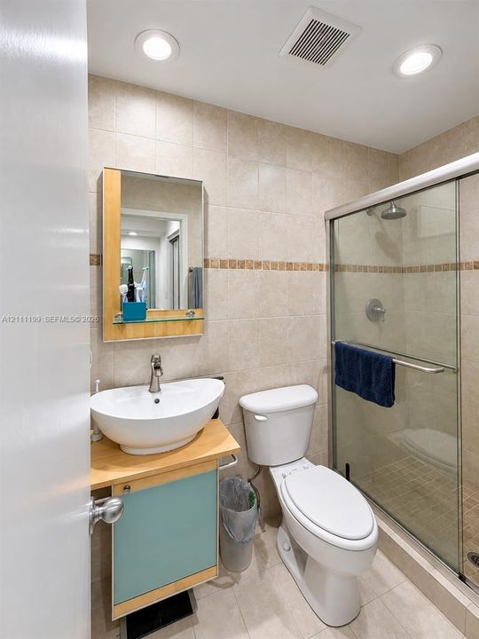 Bathroom featuring a vessel sink with a silver-finish faucet, wall-mounted medicine cabinet with a wood-tone frame, tiled shower enclosure with a glass door, and recessed lighting