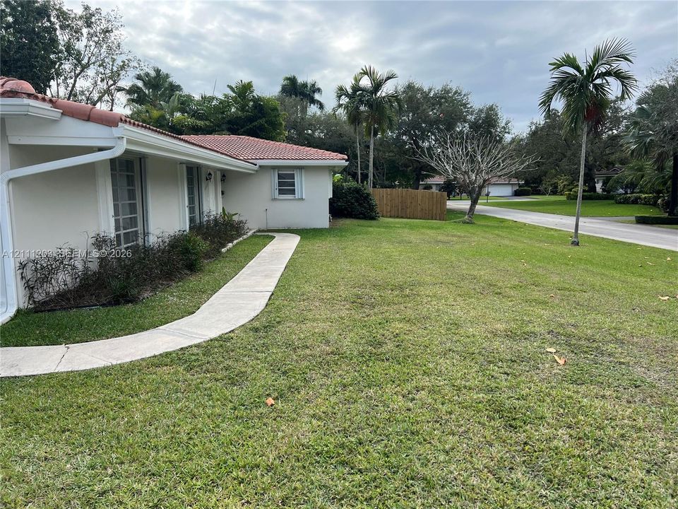 Stucco exterior featuring a clay tile roof, concrete walkway, and landscaped lawn with mature palm trees