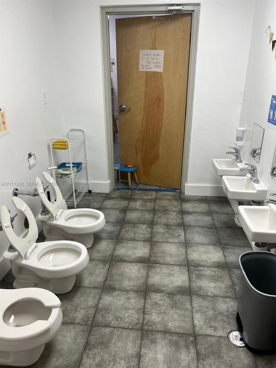 Restroom featuring three wall-mounted toilets, three wall-mounted sinks with chrome faucets, and stone-finish floor tiling