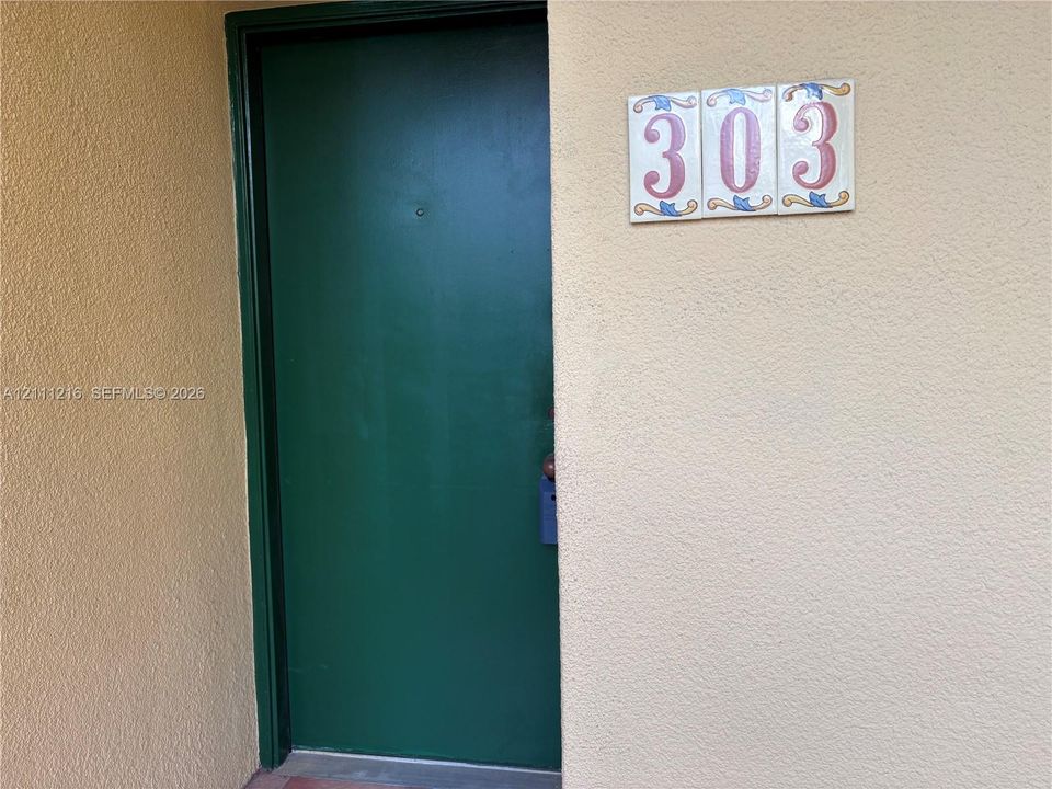 Solid green entrance door with a peephole and decorative ceramic numeric signage
