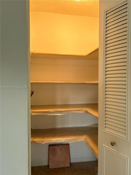 Storage space featuring tiered shelving and louvered door access