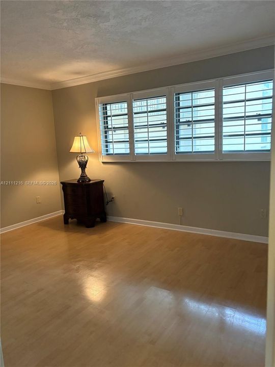 Interior space featuring wood-finish flooring, multi-pane windows with integrated white plantation shutters, and crown molding