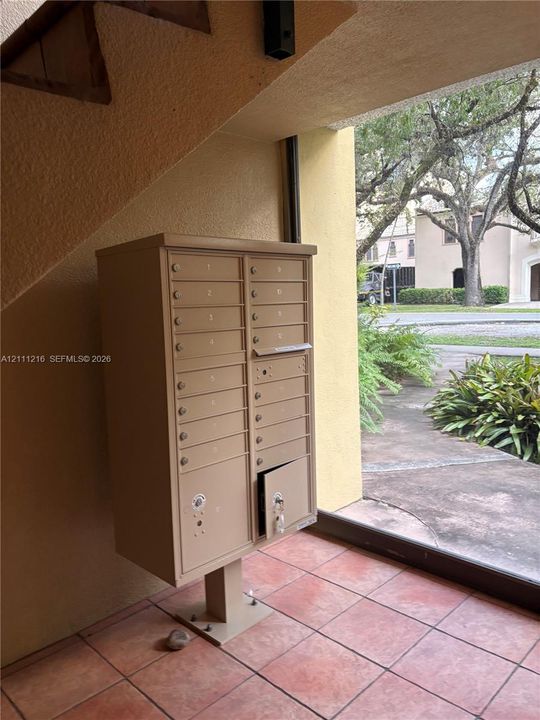 Covered mail station featuring a tan metal multi-unit mailbox console situated on terracotta-style tile flooring