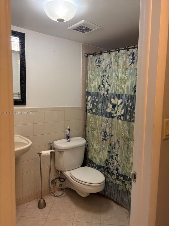 Bathroom featuring tile wall cladding, wall-mounted porcelain sink, ceramic tile flooring, and a flush-mount ceiling light fixture