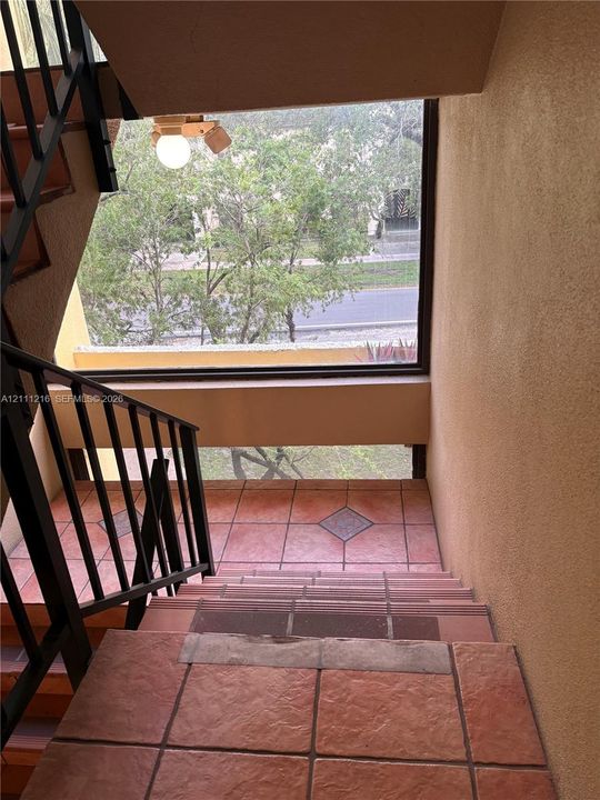 Staircase featuring textured terracotta-toned tile flooring, diamond-patterned tile accents, and black metal railings