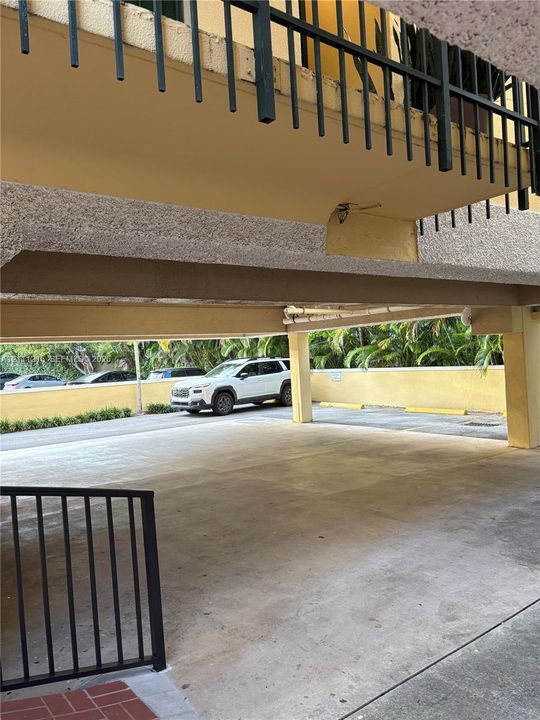 Covered parking area featuring concrete flooring, structural support pillars, and black metal railings