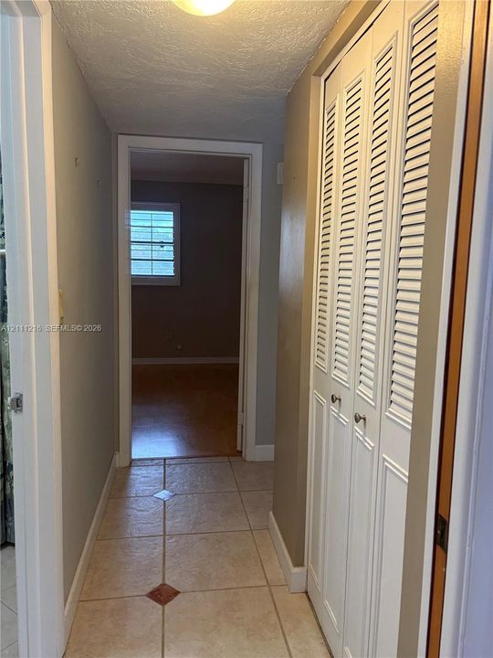 Hallway featuring light-colored tile flooring with decorative inlay accents and white louvered bi-fold closet doors