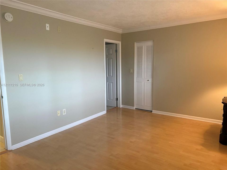 Interior space featuring wood-finish flooring, neutral wall paint, white crown molding, and a louvered bi-fold closet door