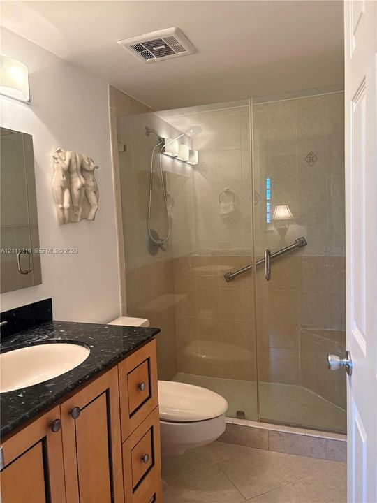 Bathroom featuring a vanity with a stone countertop and an undermount sink, paired with a glass-enclosed shower with tiled surround and an integrated bench