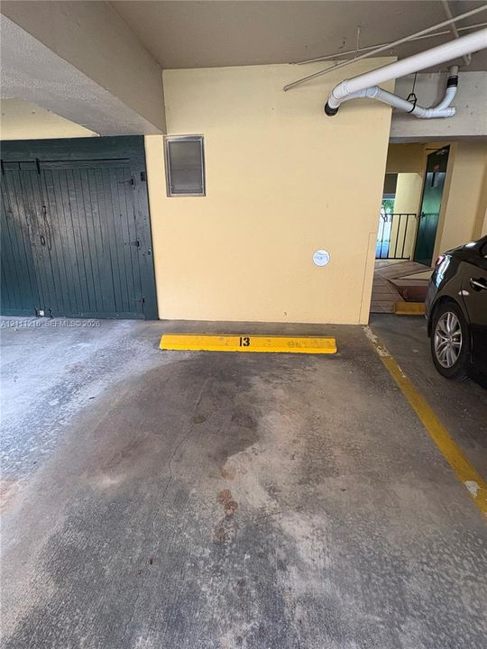 Covered parking space featuring a concrete surface, dedicated yellow wheel stop, and nearby built-in storage unit