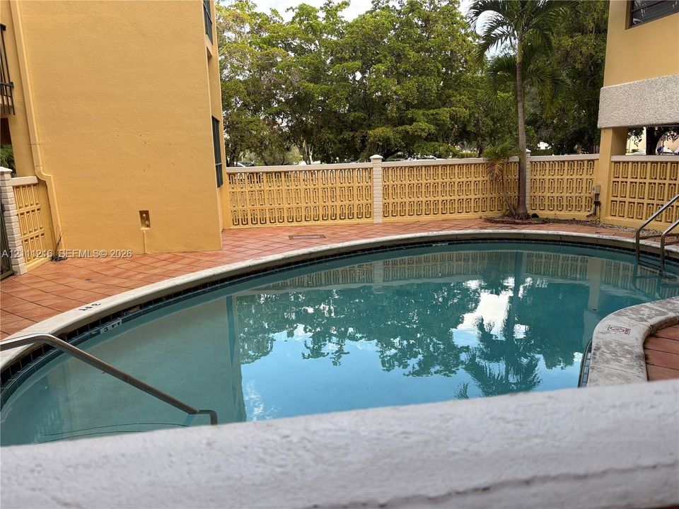 In-ground swimming pool with tile surround, decorative masonry privacy wall, and metal handrails