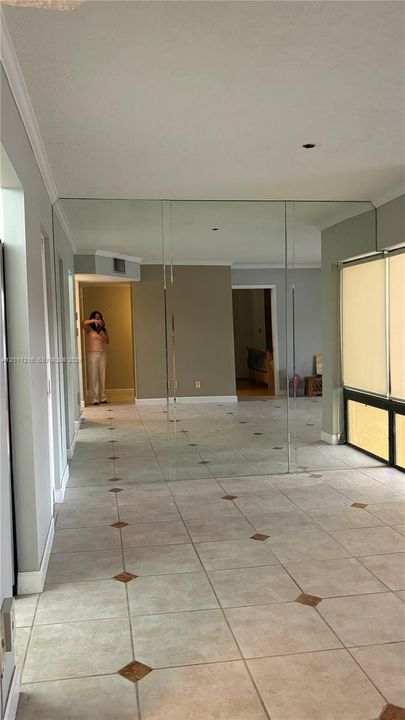 Tile flooring with decorative inset accents, wall-to-wall mirrored paneling, and large windows with horizontal blinds