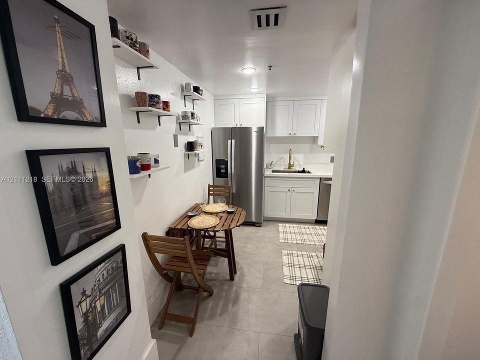 Kitchen featuring white cabinetry, stainless steel refrigerator, stone-composite countertops, built-in wall shelving, and tile flooring