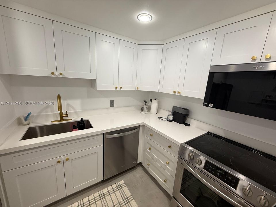 Kitchen featuring white shaker-style cabinetry, solid-surface countertops, stainless steel appliances, and brass-tone hardware