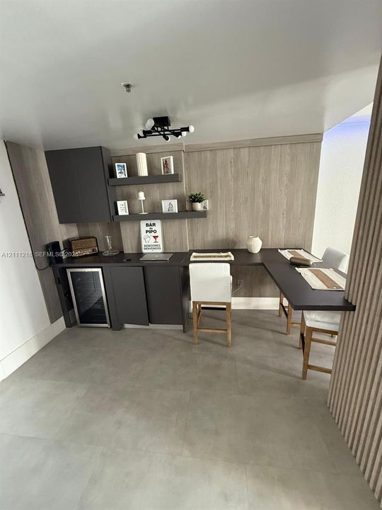 Custom cabinetry featuring matte charcoal doors, wood-finish wall paneling, integrated under-counter beverage refrigerator, floating shelves, and an extended workspace surface